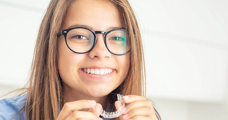 Young girl smiling and holding Invisalign